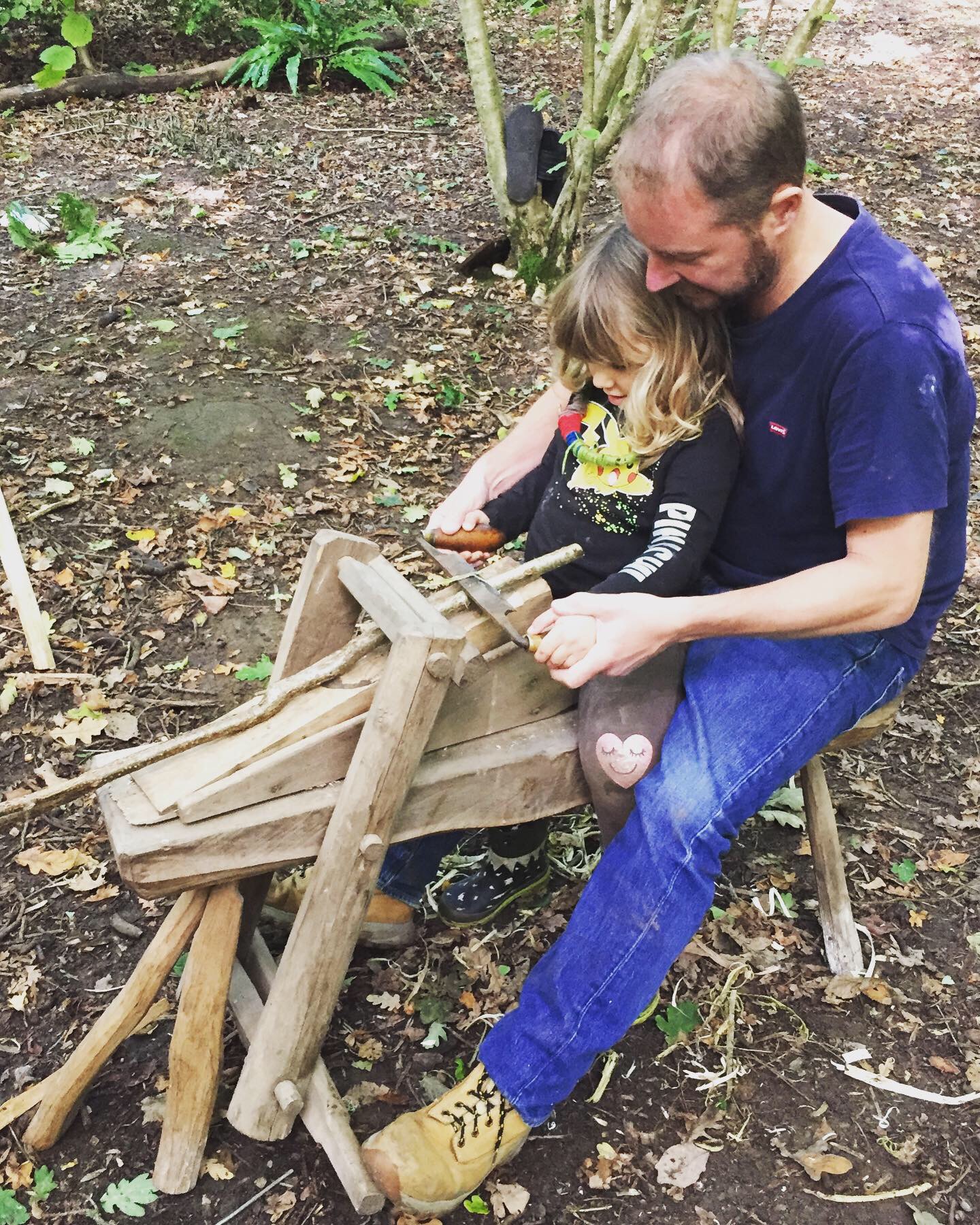 Sam Bennett sharing shave-horse woodworking with his child in the woodland